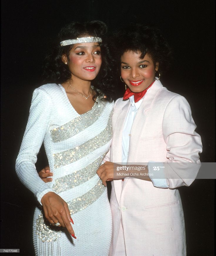 two women standing next to each other in front of a black background and one wearing a white dress