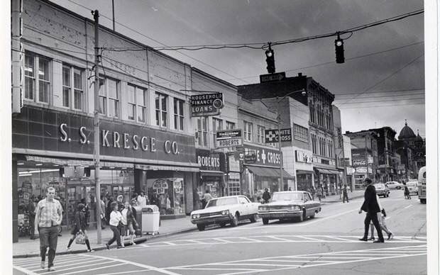 an old black and white photo of people crossing the street in front of store fronts