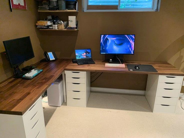 a desk with two computers on it in front of a window and some other items