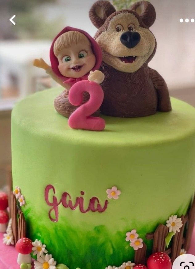 there is a birthday cake with a teddy bear and girl on the top it's green frosting