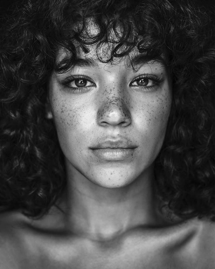 a black and white photo of a woman with freckles on her face looking at the camera