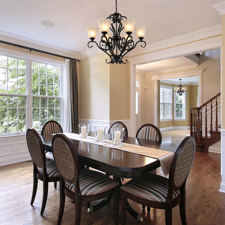 a dining room table with chairs and a chandelier hanging from the ceiling in front of two windows