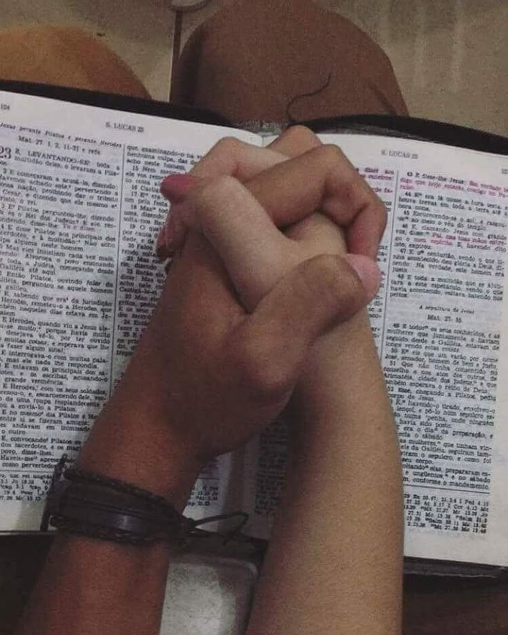 two hands clasped over an open bible