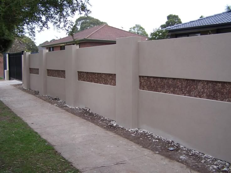 a concrete fence with some rocks on the side and grass in front of it next to a sidewalk