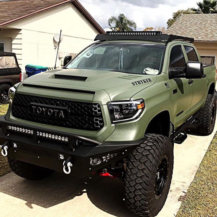 a green truck is parked in front of a house with two other trucks behind it