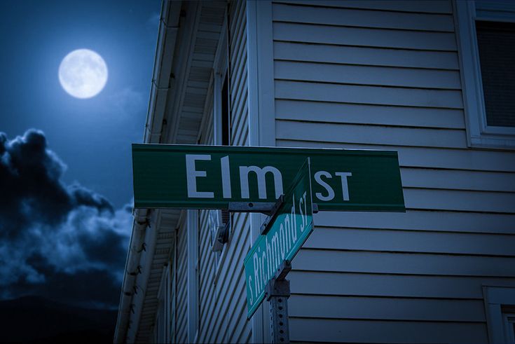 two green street signs sitting on the side of a building under a moon lit sky