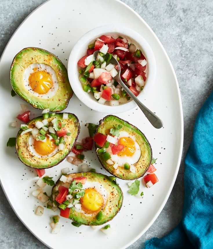 an avocado with eggs and salsa on a white plate