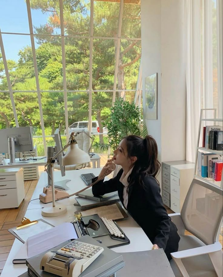 a woman sitting at a desk in front of a window with a laptop computer on it