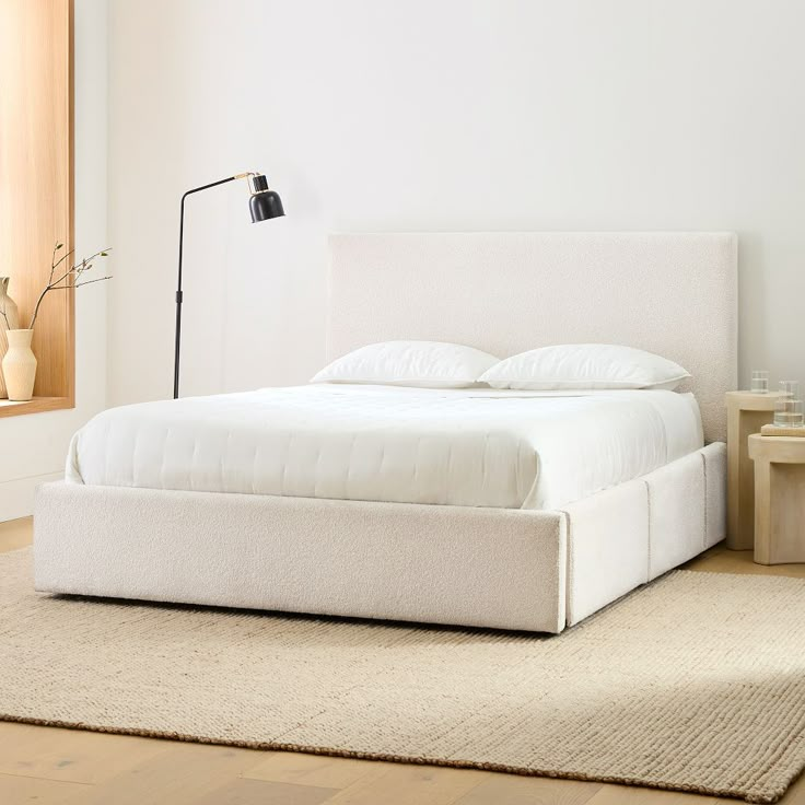 a white bed sitting on top of a wooden floor next to a lamp and window