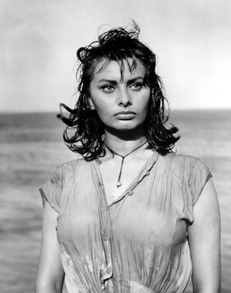 a black and white photo of a woman in front of the ocean with her hands on her hips