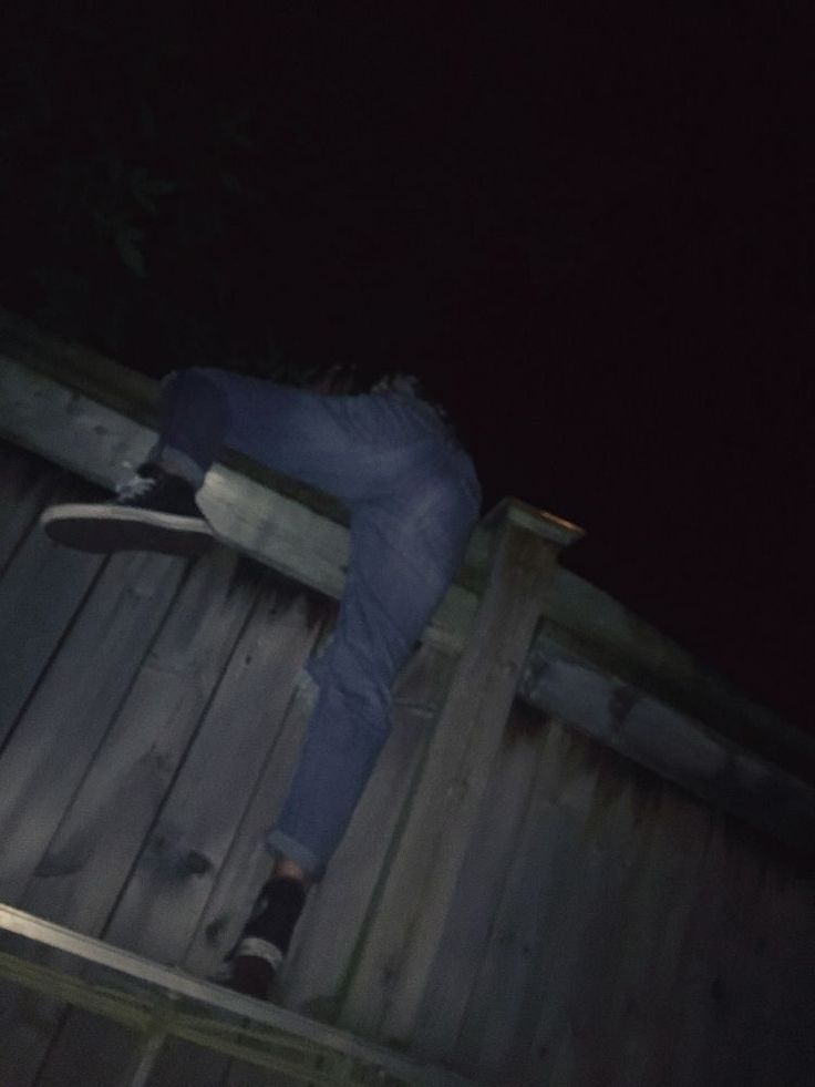 a man riding a skateboard down the side of a wooden fence at night time