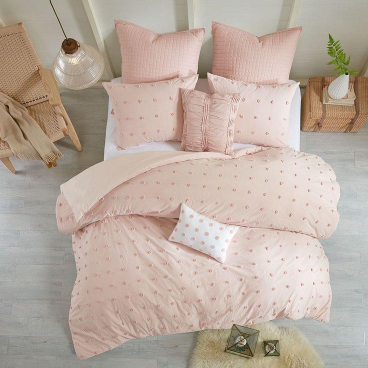 a bed with pink comforters and pillows in a white room next to a window