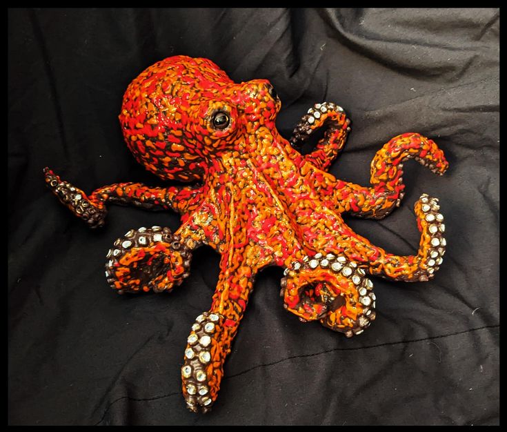 an orange and white octopus laying on top of a black cloth covered bedding area