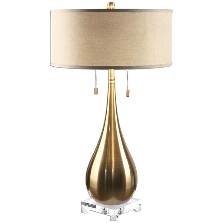 a table lamp with a white shade on it and a gold base, sitting next to a light bulb