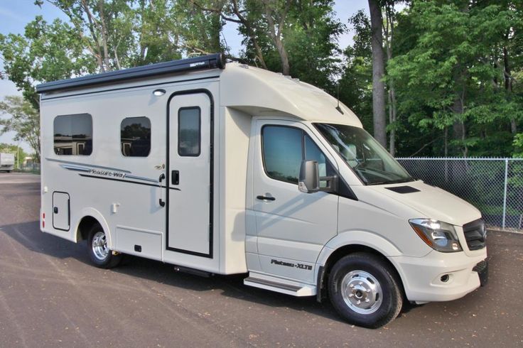 an rv parked in a parking lot next to a chain link fence with trees behind it