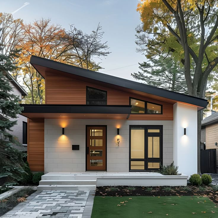 This stylish Scandinavian bungalow features a striking sloped roof and a blend of white stucco and wood siding. Large windows and a sleek door, flanked by minimalist wall lights, enhance the modern facade. The front yard boasts a paved walkway and a lush lawn, complementing the clean lines and natural materials. This design beautifully merges traditional Scandinavian elements with contemporary architecture, making it a perfect blend of elegance and modernity. Two Story Slanted Roof House, One Side Roof House Design, White House With Wood Posts, White And Wood Modern House, House Design Wood Modern, Skillion Roof Facade Modern Exterior, Country Home Designs Exterior, White House Natural Wood Trim Exterior, Modern House Exterior Materials