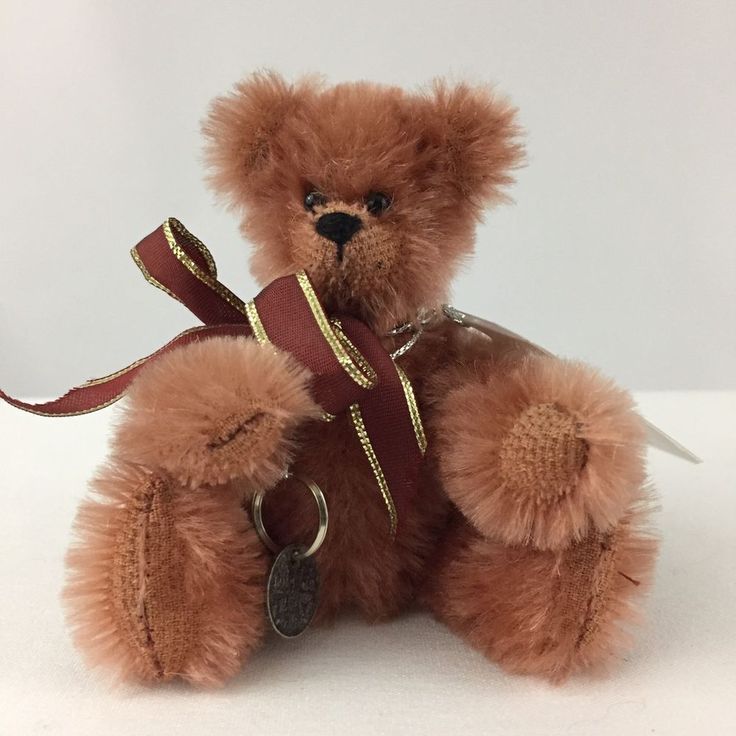 a brown teddy bear with a red ribbon around it's neck sitting on a white surface