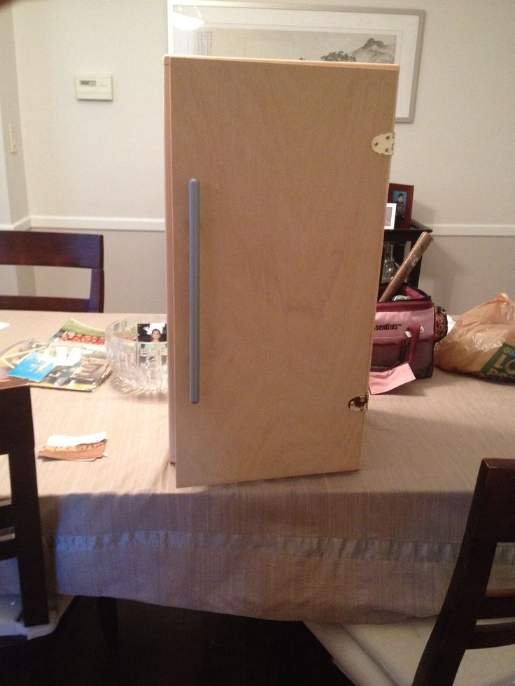 a wooden refrigerator sitting on top of a table next to a bag of food and a chair