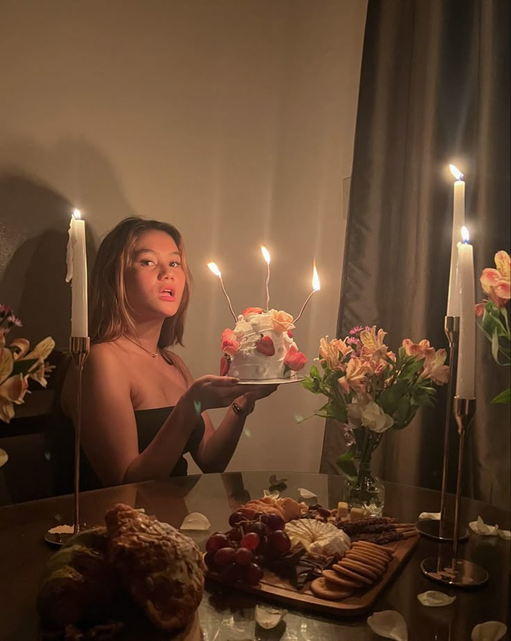 a woman holding a cake with candles on it in front of flowers and other food