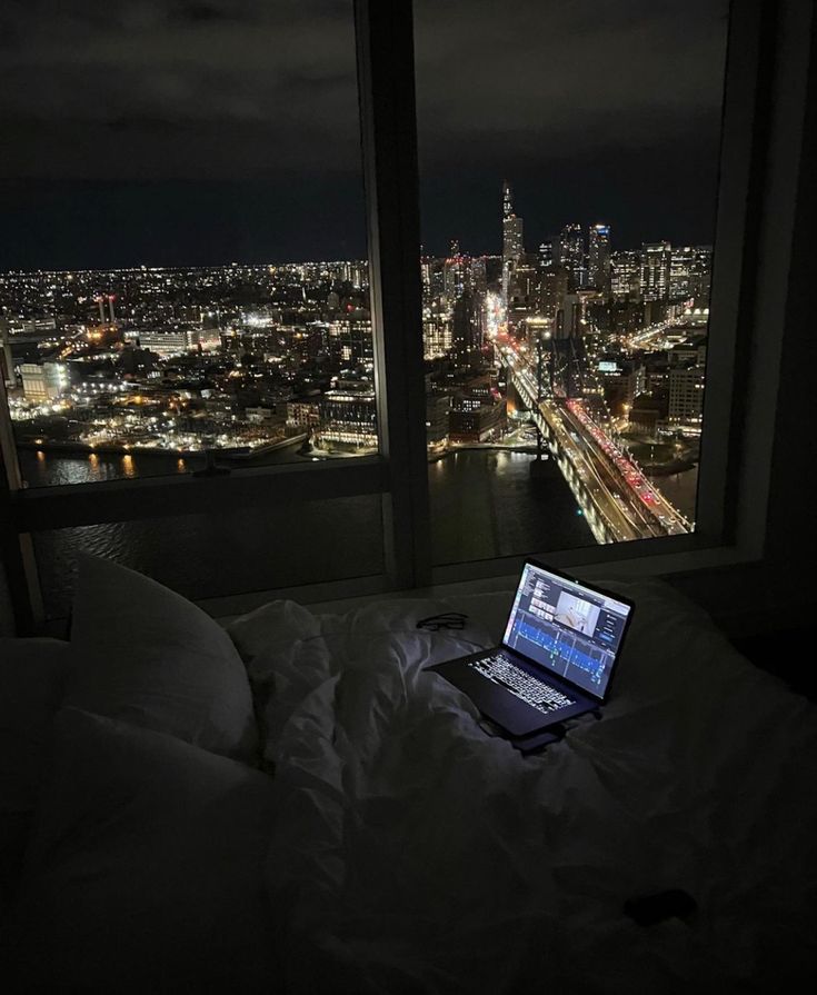 an open laptop computer sitting on top of a bed in front of a large window