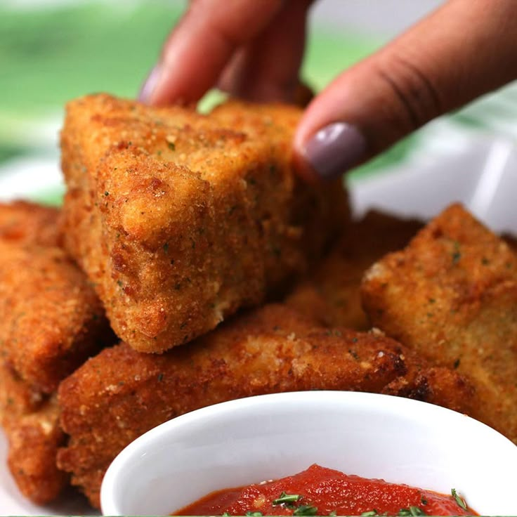 someone is dipping something into a small white bowl with sauce on the side and another hand reaching for it