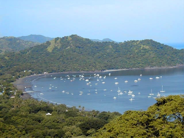 many boats are in the water near some hills and trees with mountains in the background