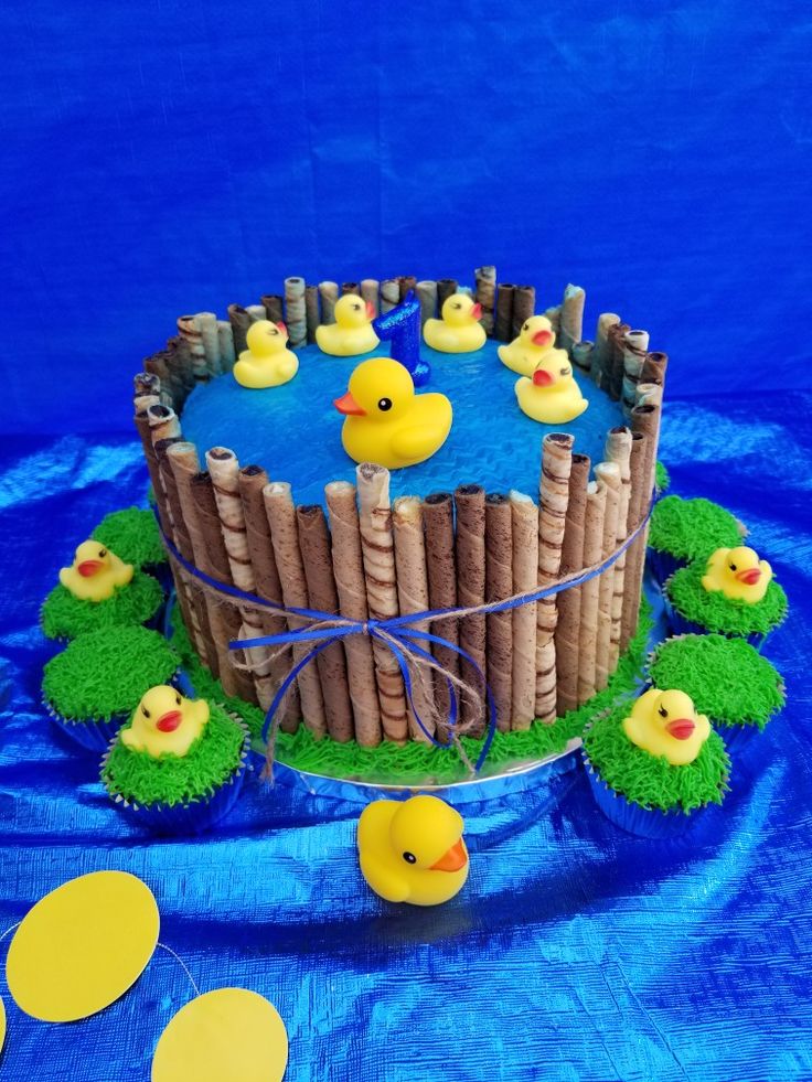 a cake decorated with rubber ducks and fenced in grass on a blue tablecloth