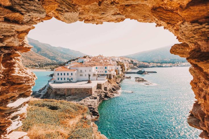 the view from inside an arch looking out to sea and buildings on land with mountains in the background