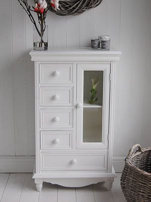 a white cabinet with glass doors and drawers in a room next to a wicker basket