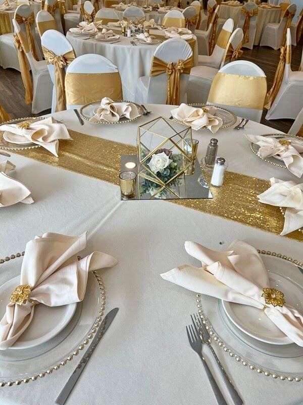 the table is set with white and gold linens, silverware, and napkins