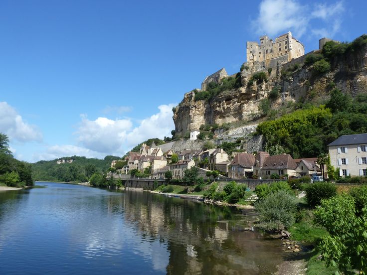 a river running through a lush green hillside next to a town on top of a hill