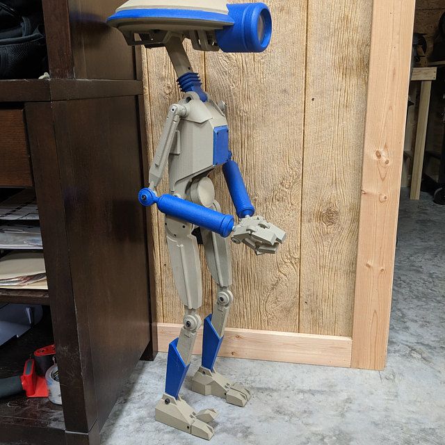 a blue and gray robot standing next to a wooden wall