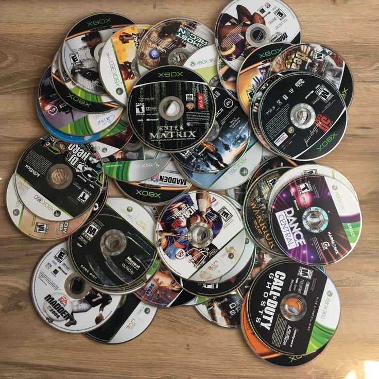 a pile of video game discs sitting on top of a wooden table next to each other