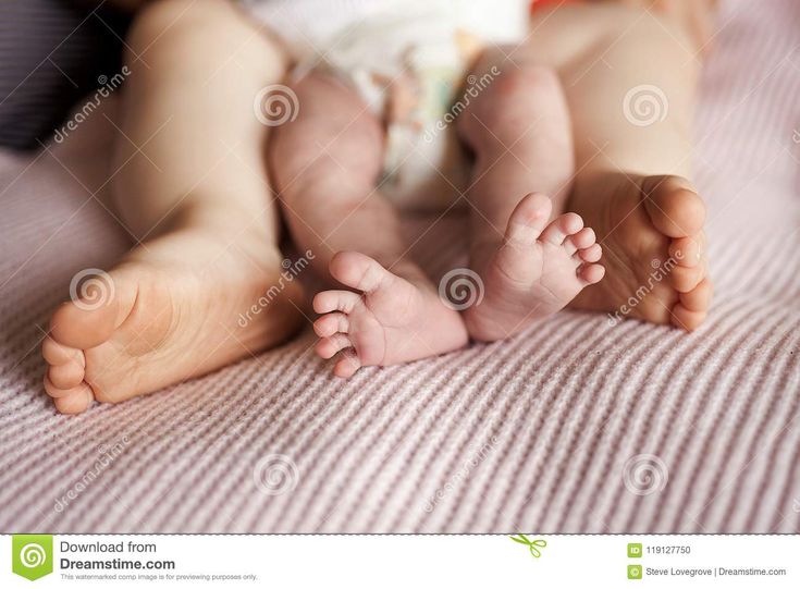 a baby laying on top of a bed next to his mother's legs and feet