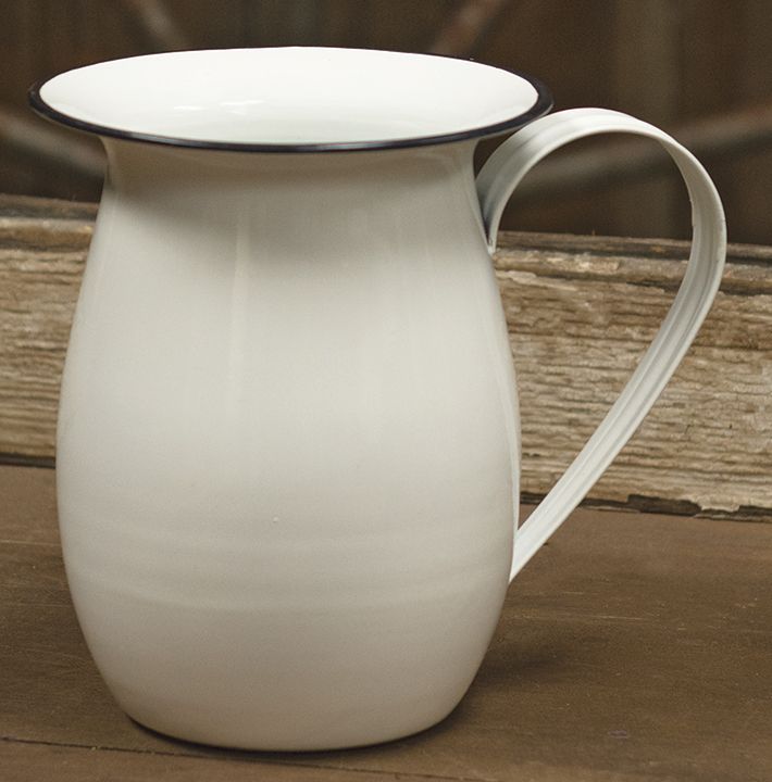 a white pitcher sitting on top of a wooden floor next to a window sill