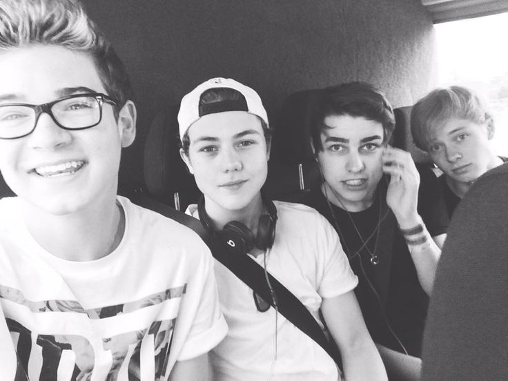 three young men sitting next to each other with headphones in their ears and one wearing a baseball cap