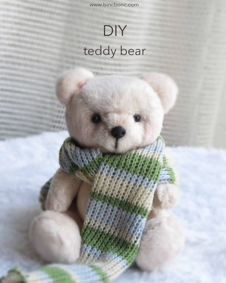 a teddy bear wearing a scarf sitting on top of a white blanket with the words diy teddy bear written above it