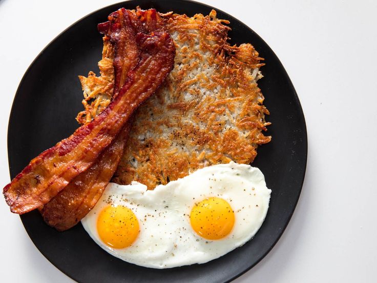 two fried eggs, bacon and hash browns on a black plate