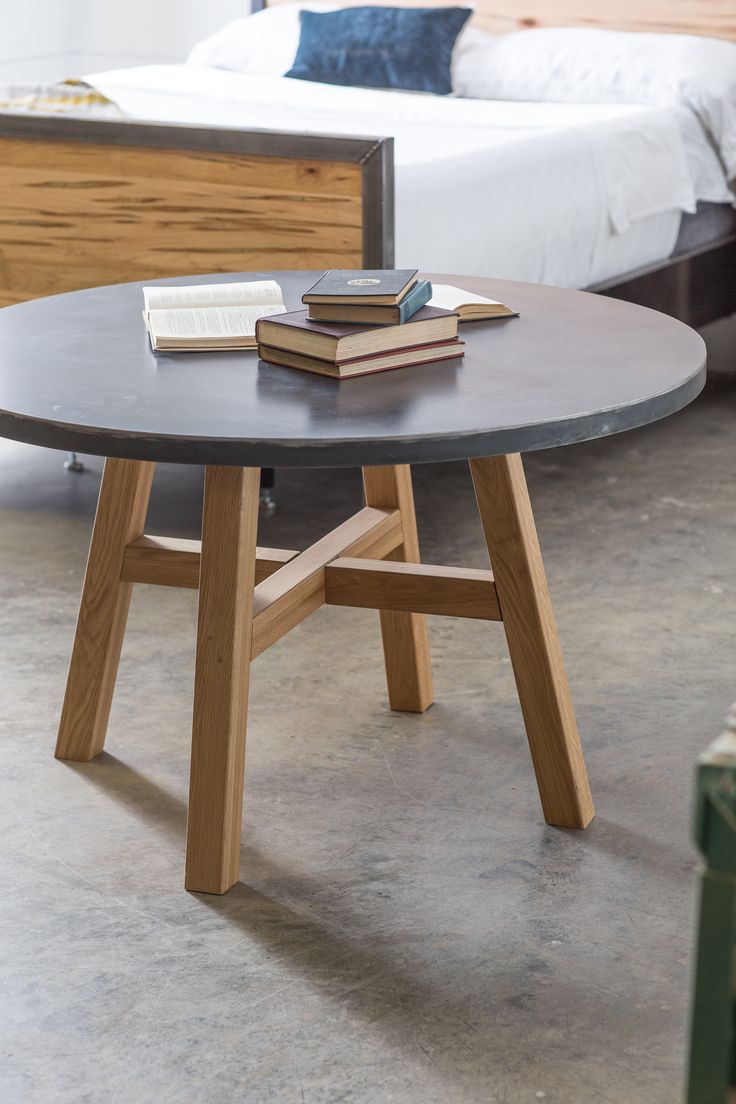 a table that has some books on it in front of a bed with a wooden headboard