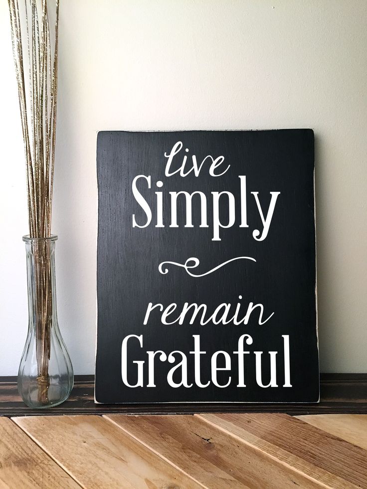 a sign that says live simply remain grateful next to a vase with dry grass in it