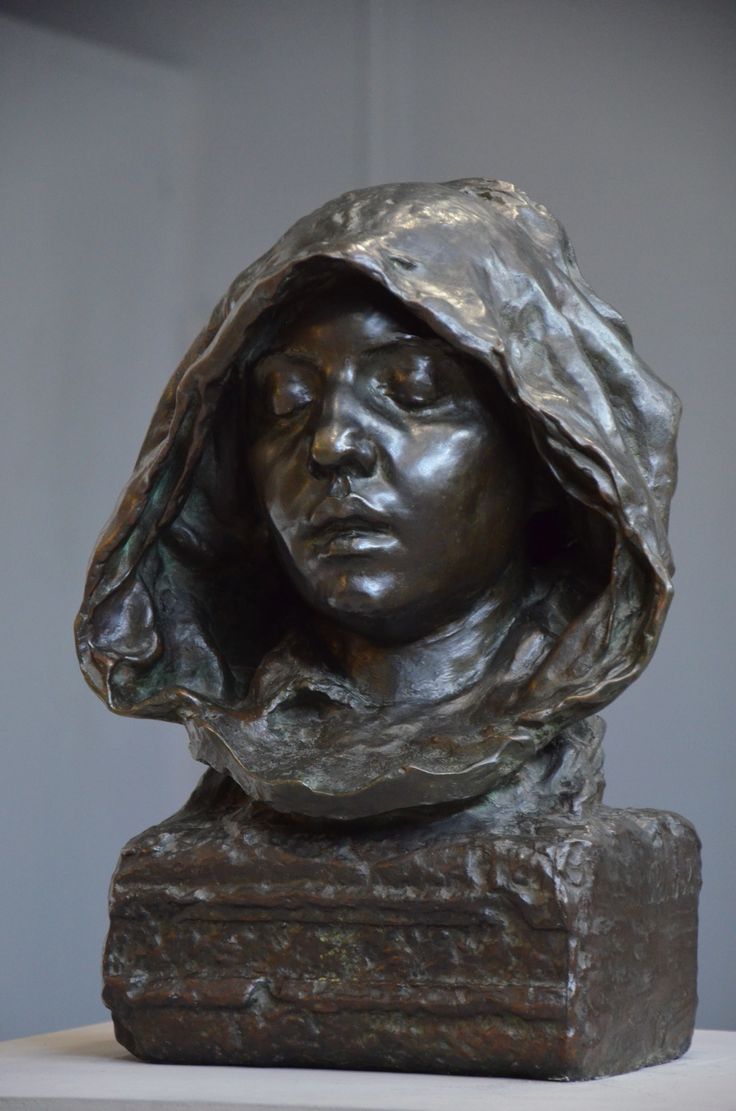 a bronze sculpture of a woman with a hood on her head, sitting on a table