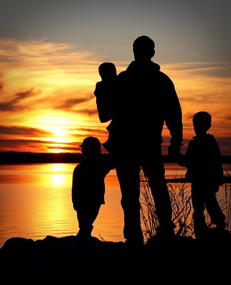 two adults and one child standing near the water at sunset