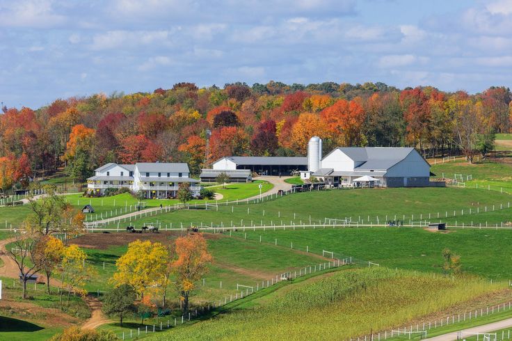 a farm surrounded by trees with fall colors in the background and a white fenced in area