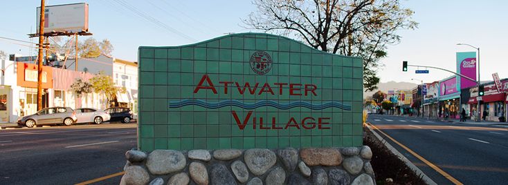 a sign that says atwater village on the side of a street with cars parked in front of it