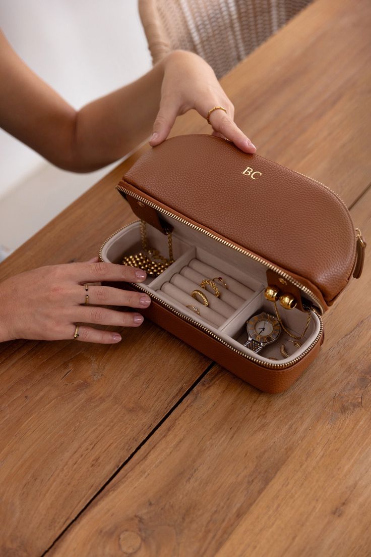 a woman is holding an open brown case with jewelry inside on a wooden table in front of her