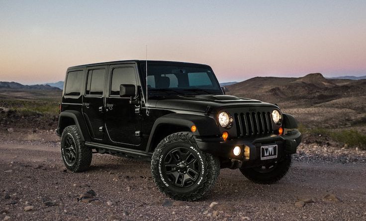 a black jeep parked in the middle of a desert road at dusk with mountains in the background