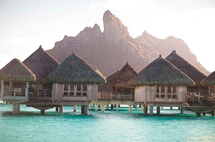 some huts that are sitting in the water near each other on stilts with mountains in the background