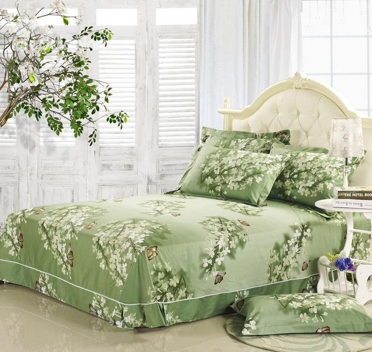 a bed sitting next to a window covered in green comforters and pillows on top of a white table