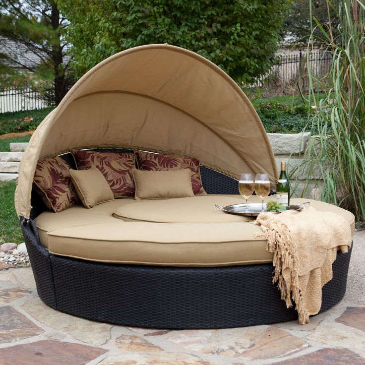 an outdoor day bed with pillows and wine glasses on the table next to it,