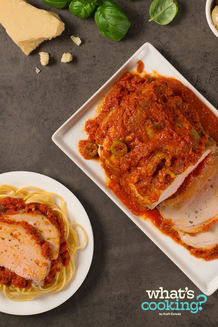 two white plates with meat and sauce on them next to some cheese, bread and basil leaves